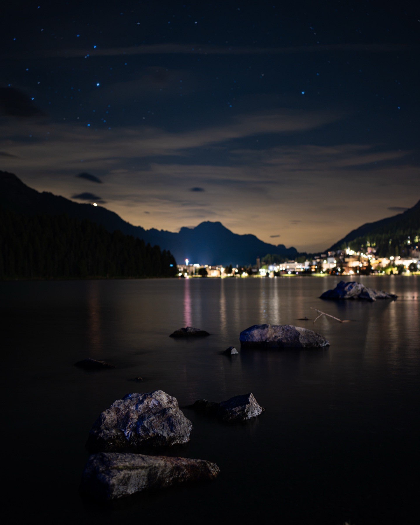 A starlit sky over the lake with village lights in the distance